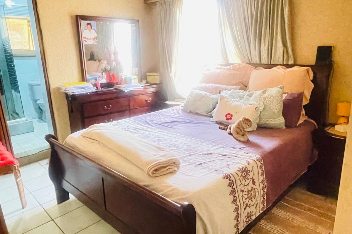 A bedroom featuring tiled flooring and an en-suite bathroom access, with natural light provided by a large window.