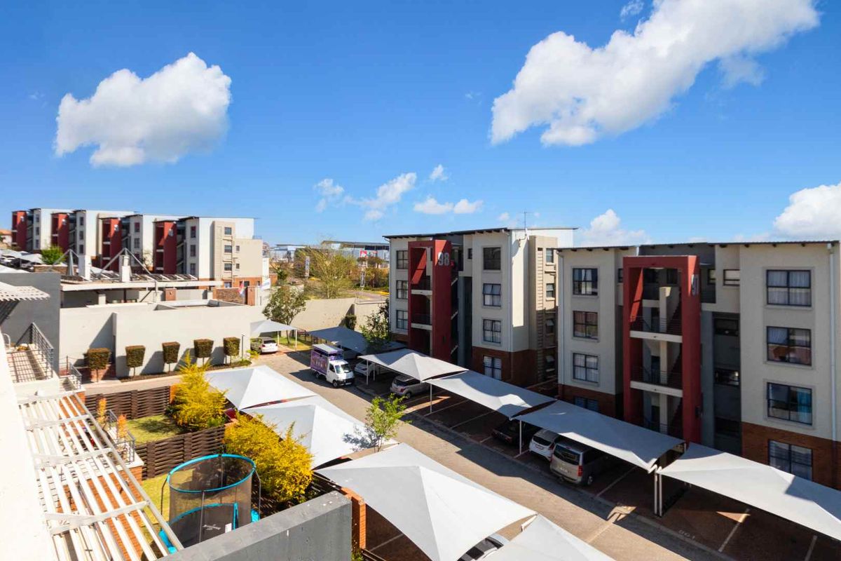 An elevated view of the apartment complex grounds, featuring covered parking bays, landscaped garden areas, and modern multi-story residential buildings.