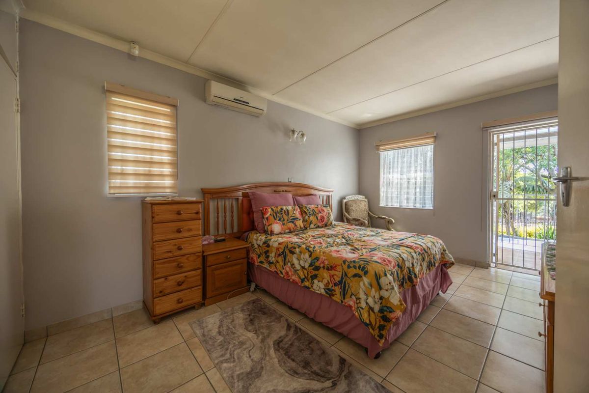 A bedroom featuring tiled flooring, a wall-mounted air conditioning unit, and direct access to an outdoor area through a security gate.