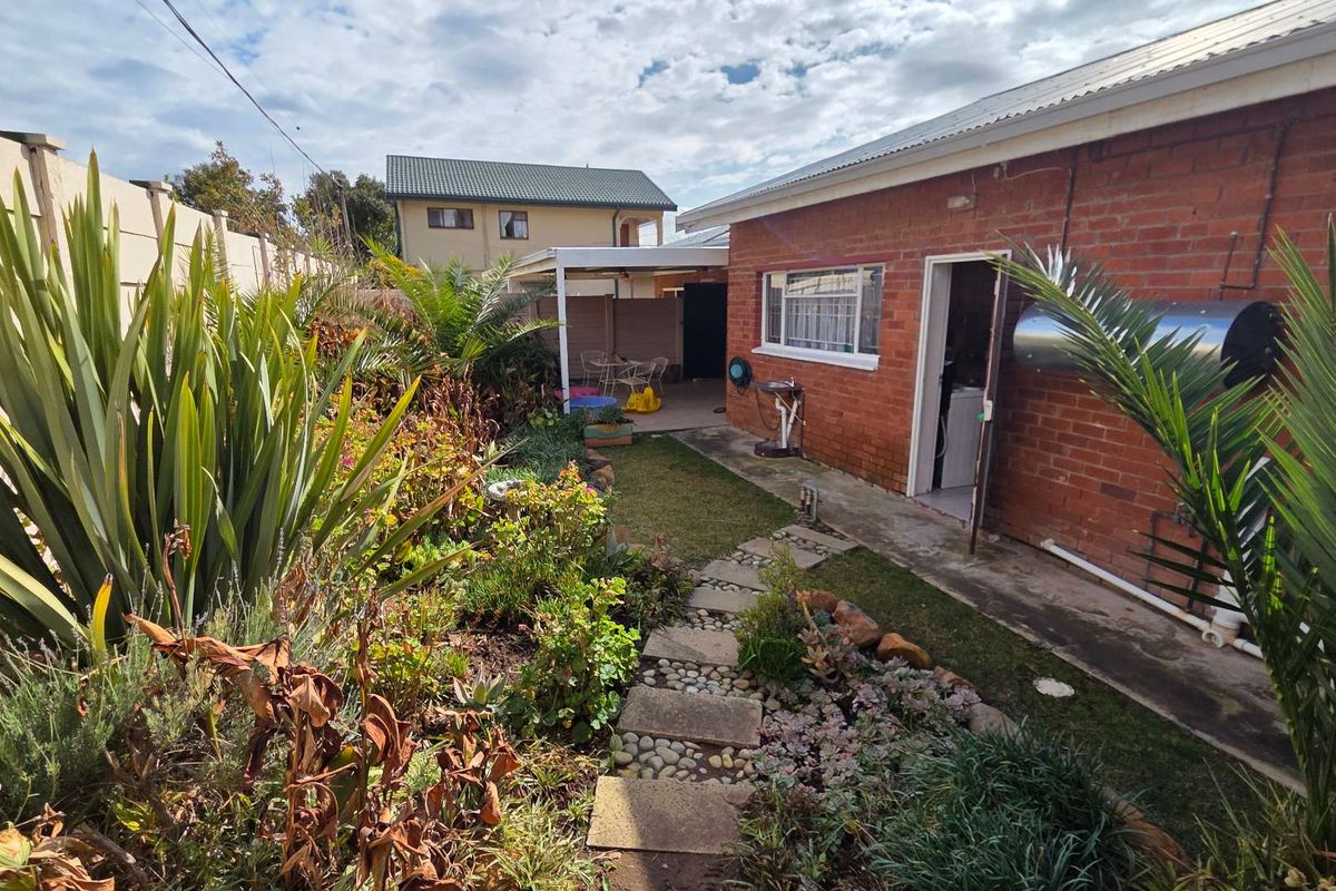 Rear exterior view of the apartment featuring a brick facade, stone pathway, established garden, and a covered patio area.