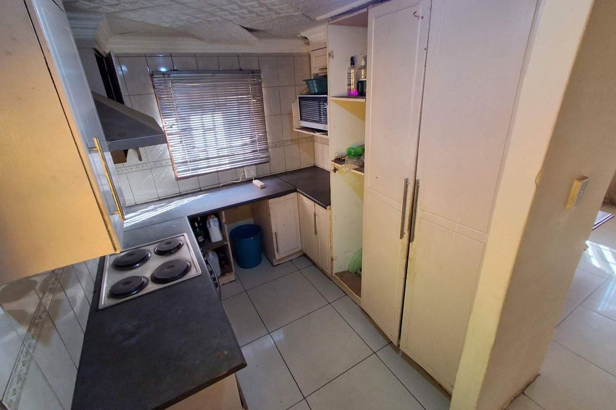 A compact kitchen featuring built-in cabinetry, an electric hob, and tiled finishes, currently showing signs of wear and requiring cosmetic updates.