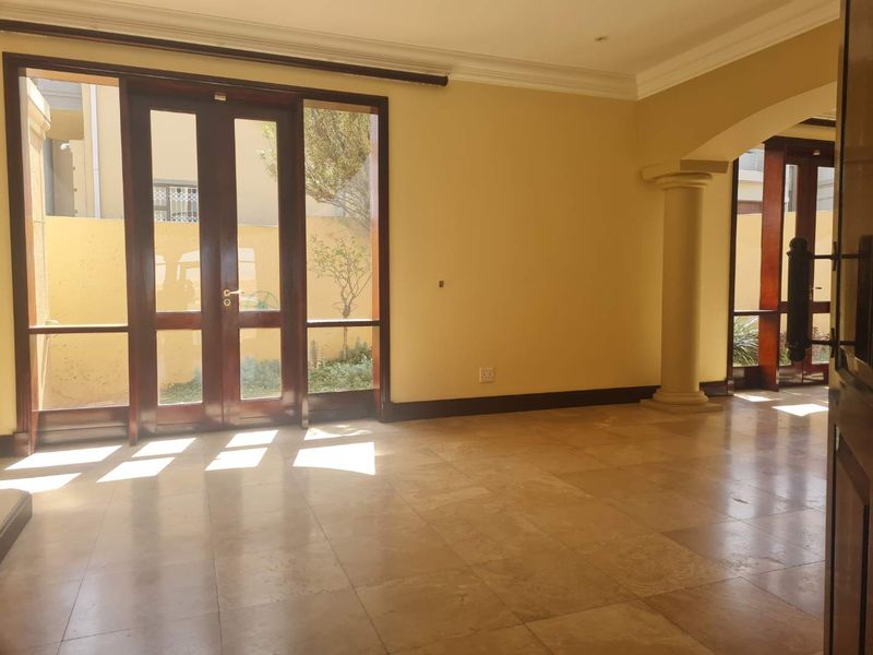 Spacious, sunlit living area featuring natural stone tile flooring, elegant wooden framed glass doors, and a decorative column leading to an adjacent space.