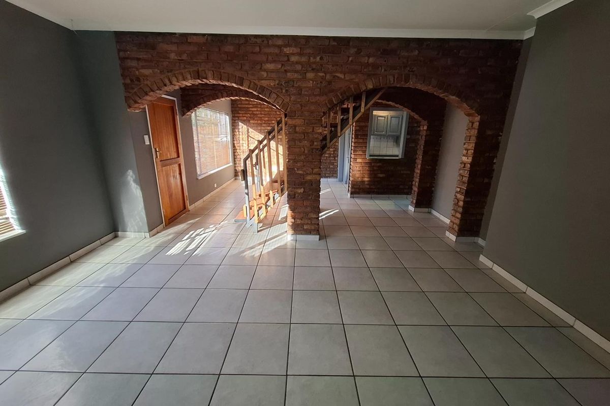 Spacious living area featuring distinctive exposed brick arches, tiled flooring, and an internal staircase, offering a unique architectural layout ready for personalization.