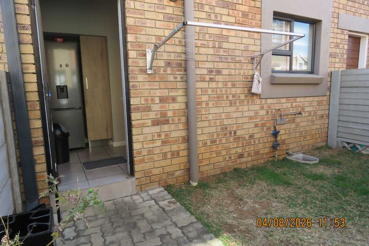 Rear exterior view of the townhouse featuring a face brick facade, paved walkway, and a wall-mounted drying rack.