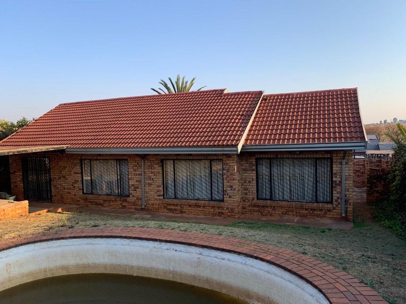 Rear view of a face brick house featuring a tiled roof, security bars on windows, and a swimming pool with brick coping.