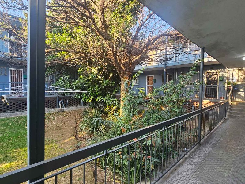 View of the apartment complex communal garden and rear walkway featuring metal balustrades and established landscaping.