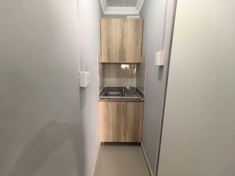 A compact and functional scullery area featuring modern wood-look cabinetry, a stainless steel sink, and a clean tiled splashback.