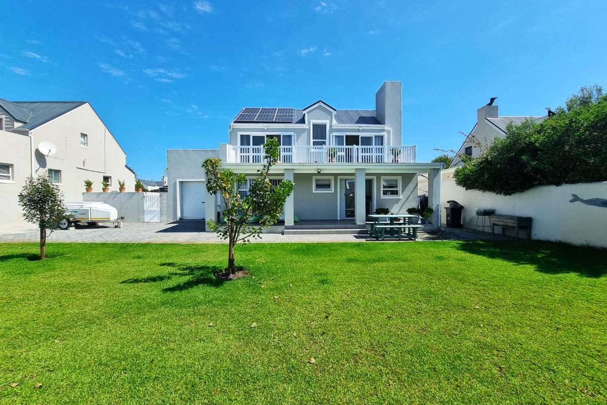 Rear view of a two-story house featuring a spacious lawn, a covered patio, a balcony, and roof-mounted solar panels.