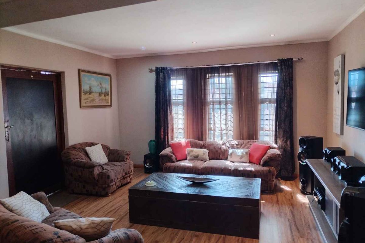 A comfortable living room featuring laminate flooring, recessed downlighting, and large windows fitted with security bars.