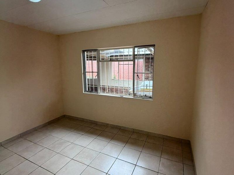 An empty bedroom featuring tiled flooring, security bars on the window, and a simple ceiling light fixture, ready for renovation or staging.