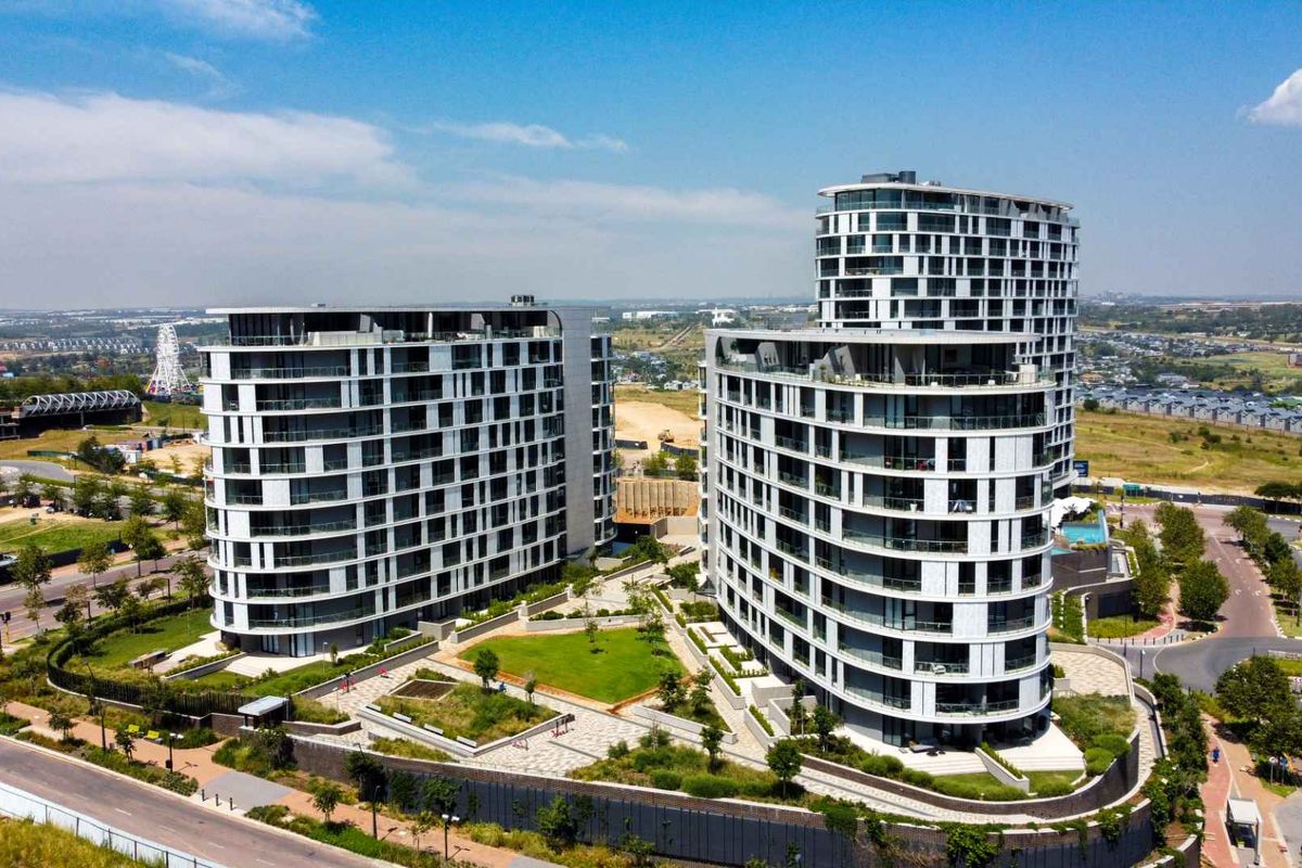 Aerial view of a modern luxury apartment complex featuring curved architectural design, landscaped gardens, and paved walkways within a secure estate.