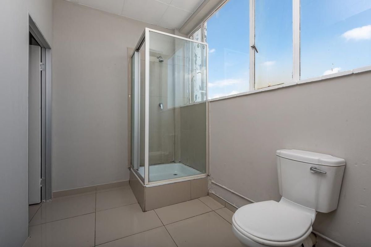 A functional bathroom featuring a glass-enclosed shower cubicle, a standard toilet, and large-format floor tiles with natural light from the window.