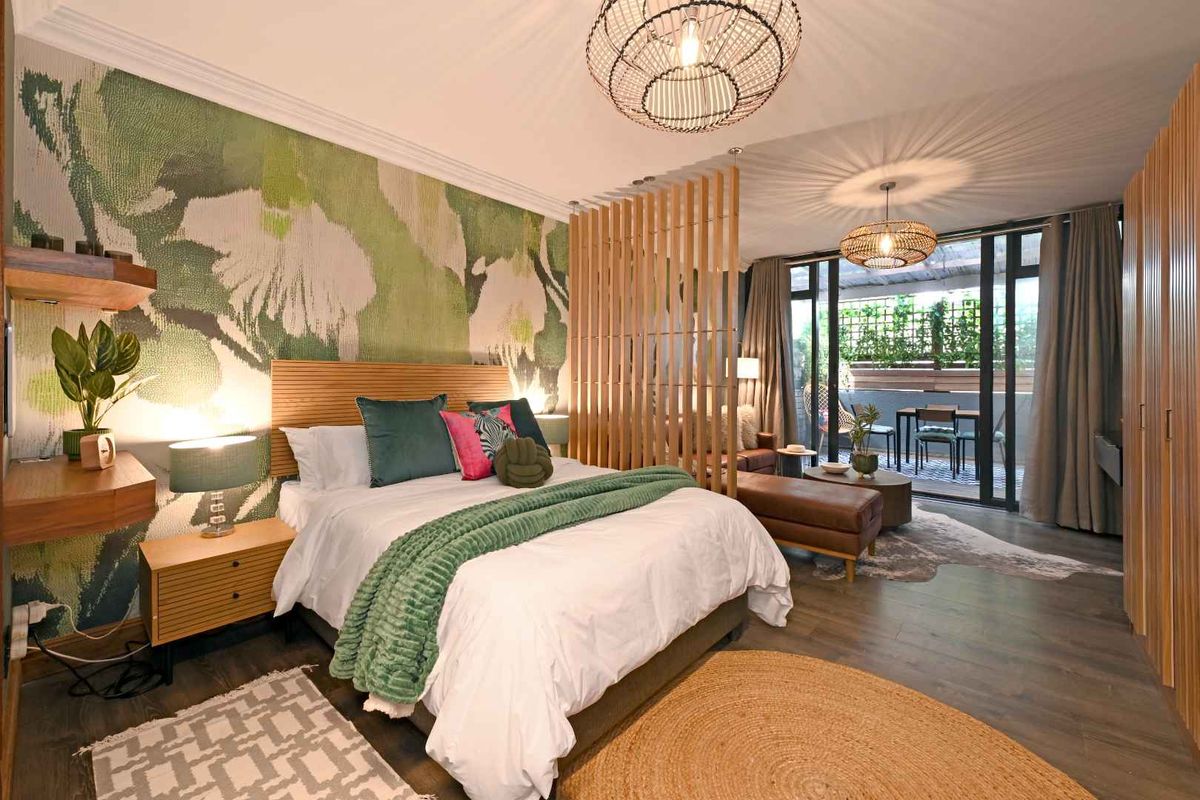 A stylish bedroom featuring a timber slat room divider, built-in wardrobes, and direct access to a private balcony through sliding glass doors.
