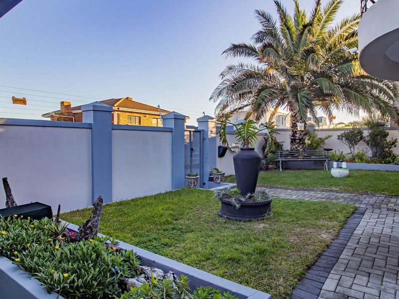 A well-maintained private garden featuring a paved walkway, manicured lawn, and secure perimeter wall with electric fencing.