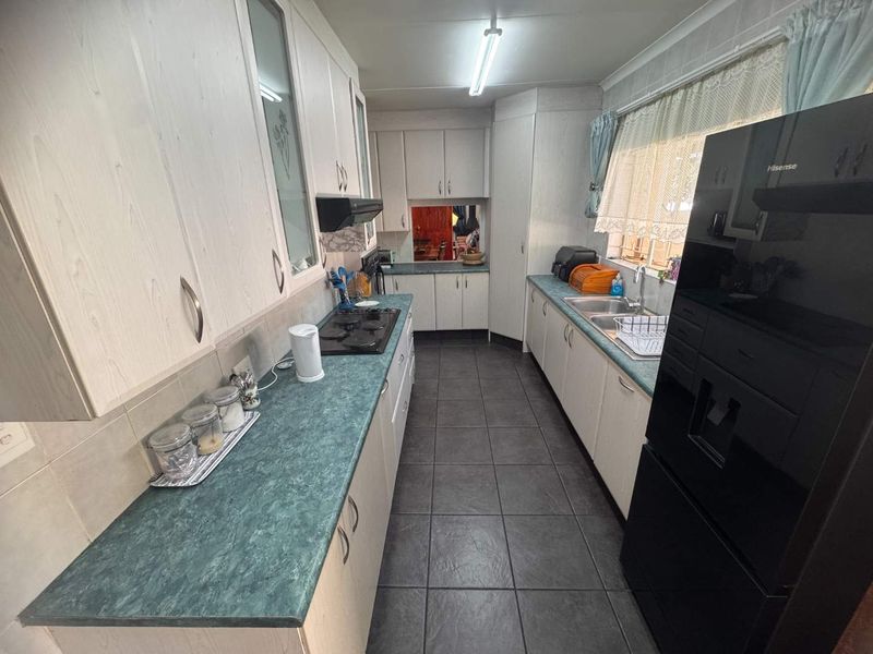 A functional galley-style kitchen featuring laminate cabinetry, green laminate countertops, a built-in hob with extractor fan, and tiled flooring.