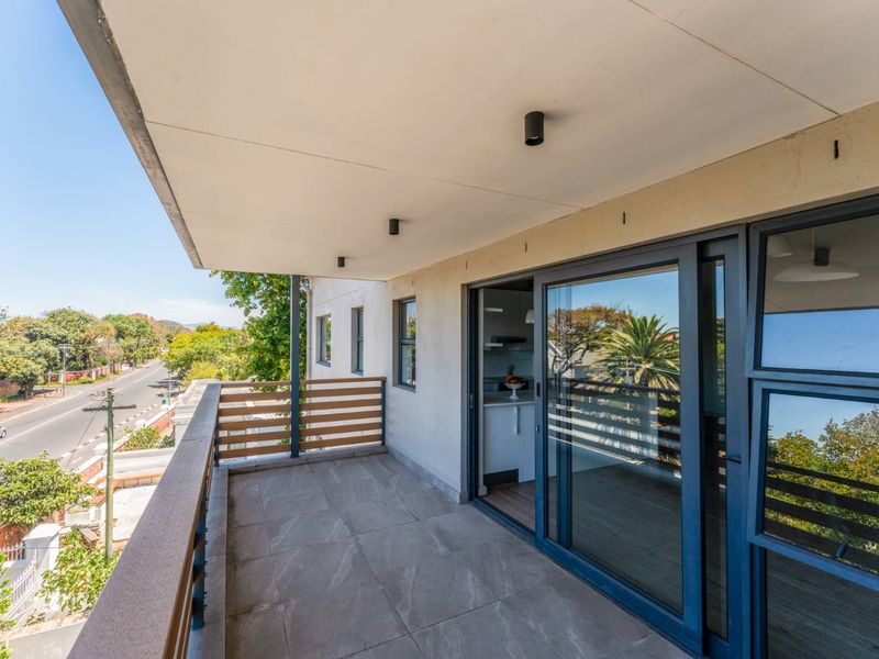 A modern, covered balcony featuring tiled flooring, a timber slat balustrade, and large sliding glass doors providing access to the interior.