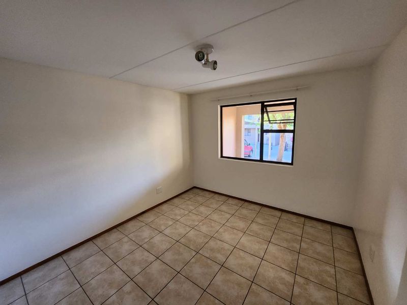 An empty bedroom featuring neutral tiled flooring, white walls, and an aluminium-framed window providing natural light.