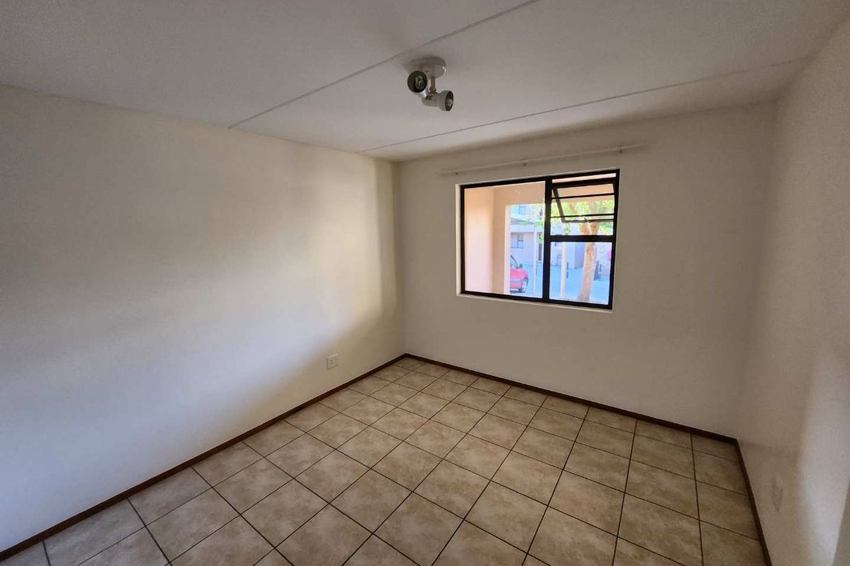 An empty bedroom featuring neutral tiled flooring, white walls, and an aluminium-framed window providing natural light.