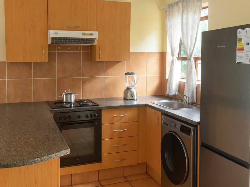 A functional kitchen featuring laminate cabinetry, granite-look countertops, built-in oven with hob, extractor fan, and integrated space for a washing machine.