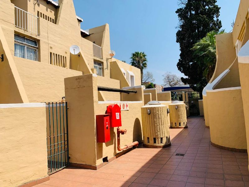 Exterior rear view of the townhouse complex featuring a tiled walkway, fire safety equipment, and multi-level balconies with yellow masonry walls.