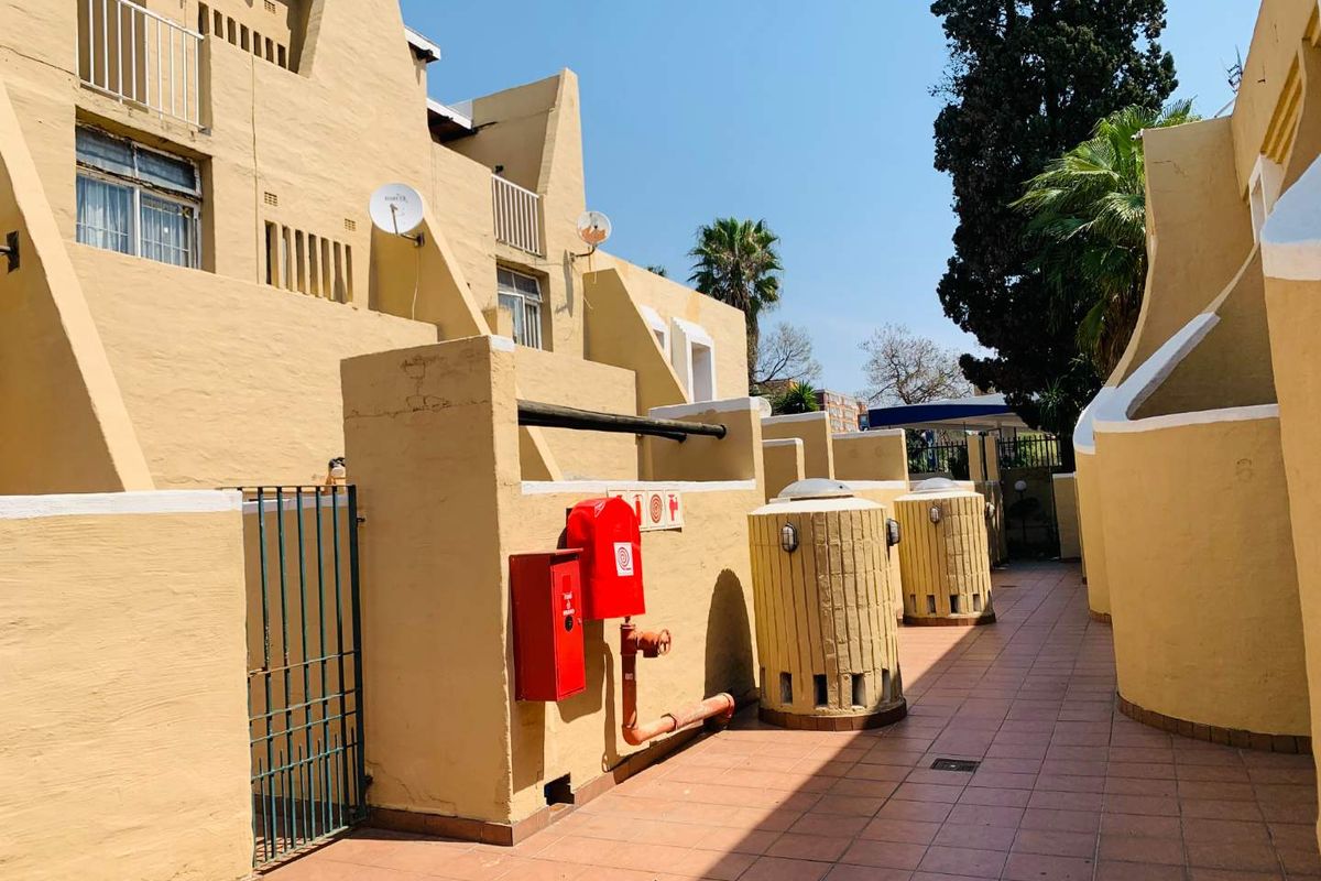 Exterior rear view of the townhouse complex featuring a tiled walkway, fire safety equipment, and multi-level balconies with yellow masonry walls.