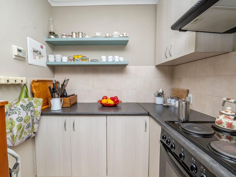 Compact kitchen featuring light wood-grain cabinetry, dark laminate countertops, a tiled backsplash, and a built-in electric stove with an extractor fan.