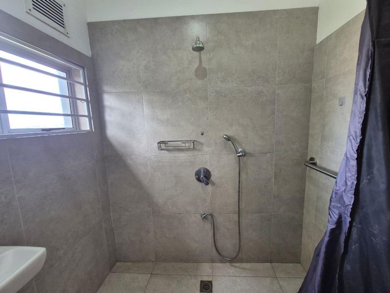 A clean, modern bathroom shower area featuring neutral grey wall tiles, a handheld shower attachment, and a fixed shower head.