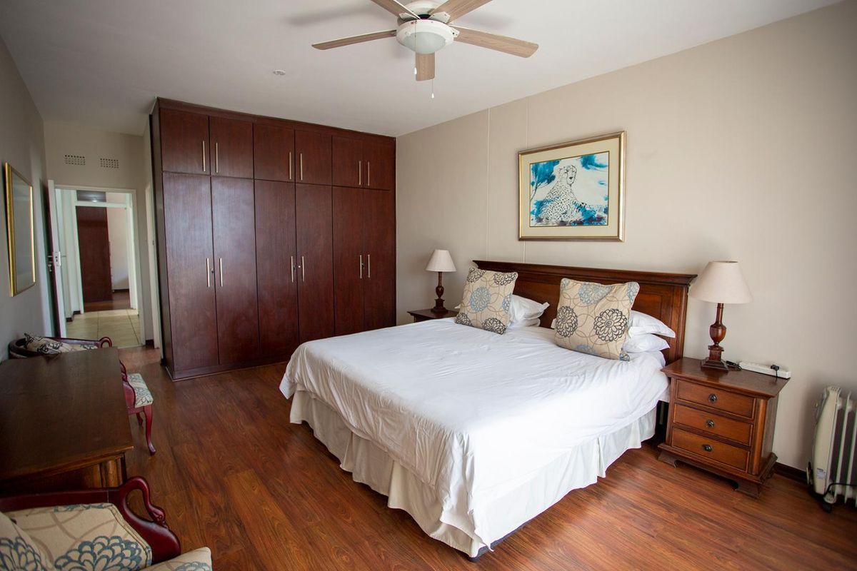 Spacious bedroom featuring dark wood built-in cupboards, laminate flooring, and a ceiling fan, offering a comfortable and well-maintained living space.