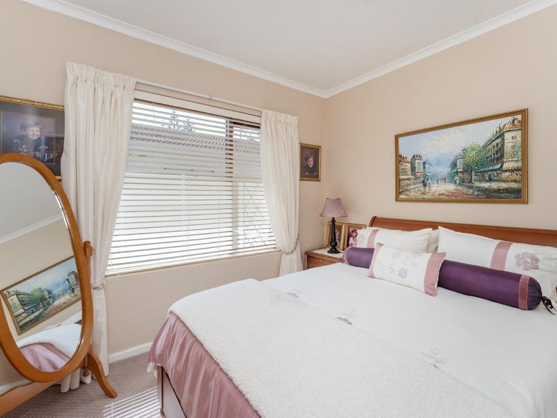 A well-maintained bedroom featuring neutral wall tones, carpeted flooring, and a window fitted with venetian blinds and curtains.