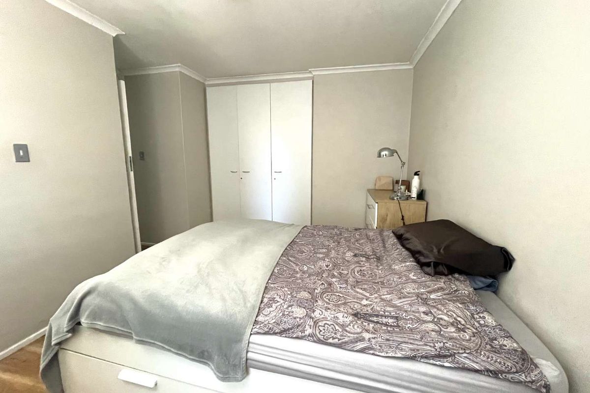 A functional bedroom featuring built-in cupboards, neutral wall finishes, and laminate flooring, providing a clean and simple living space.