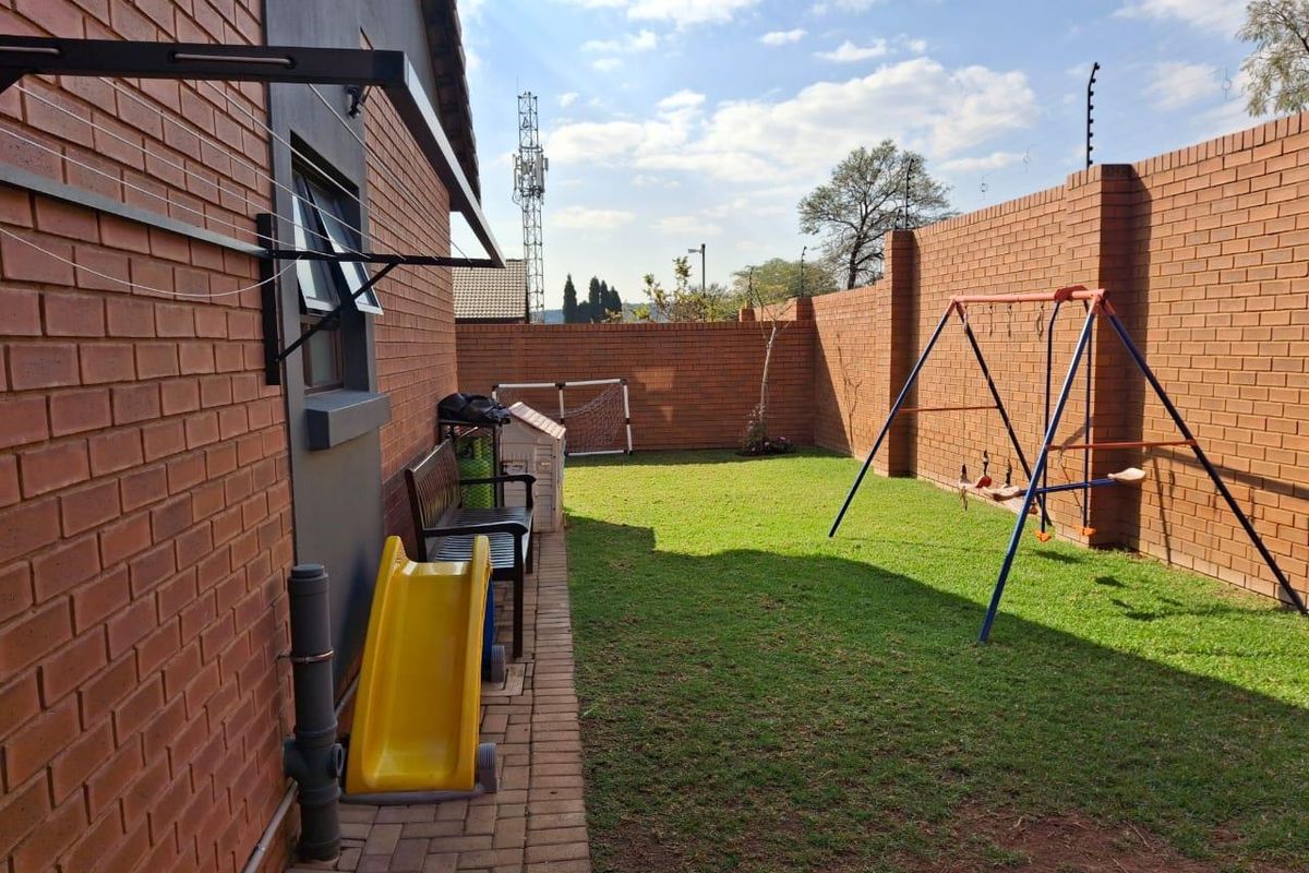 A private rear garden featuring a brick-paved walkway, a well-maintained lawn, and high perimeter brick boundary walls with electric fencing.