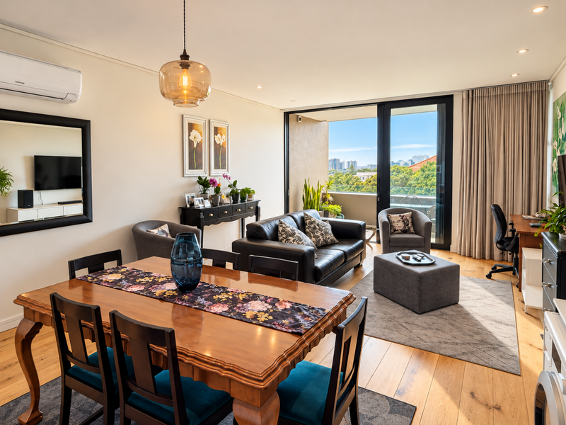 Spacious open-plan living and dining area featuring hardwood flooring, recessed lighting, and large sliding glass doors leading to a private balcony with city views.