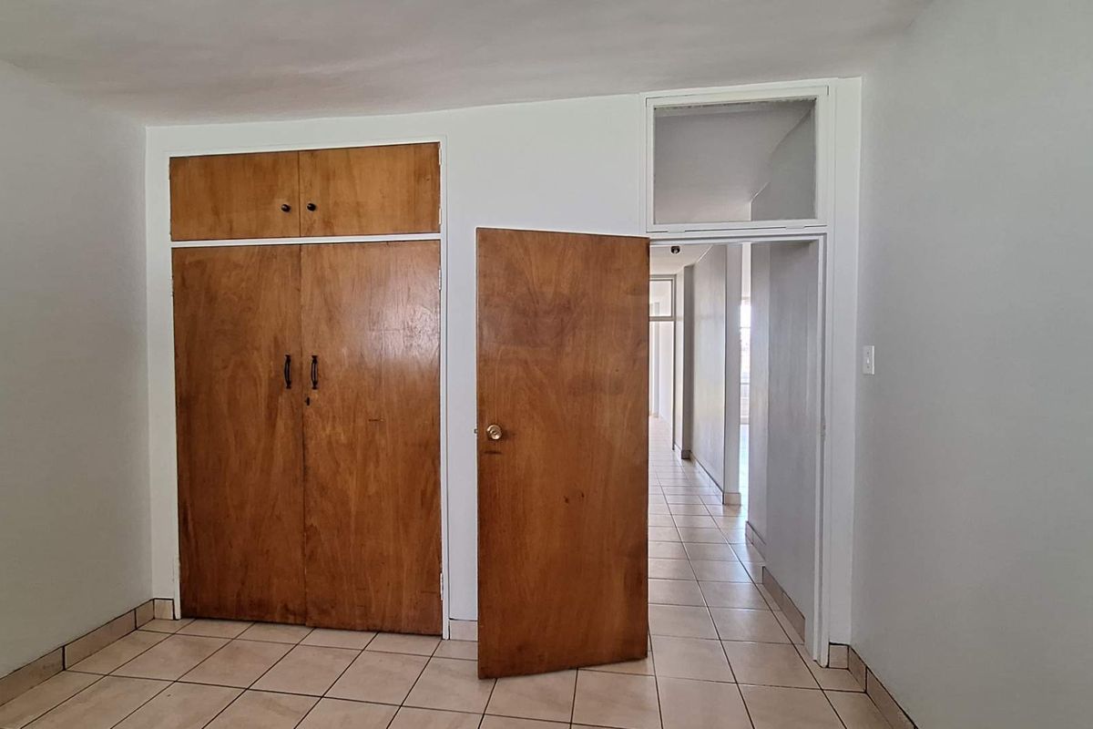 An empty bedroom featuring built-in wooden cupboards, tiled flooring, and a transom window above the doorway leading to the hallway.