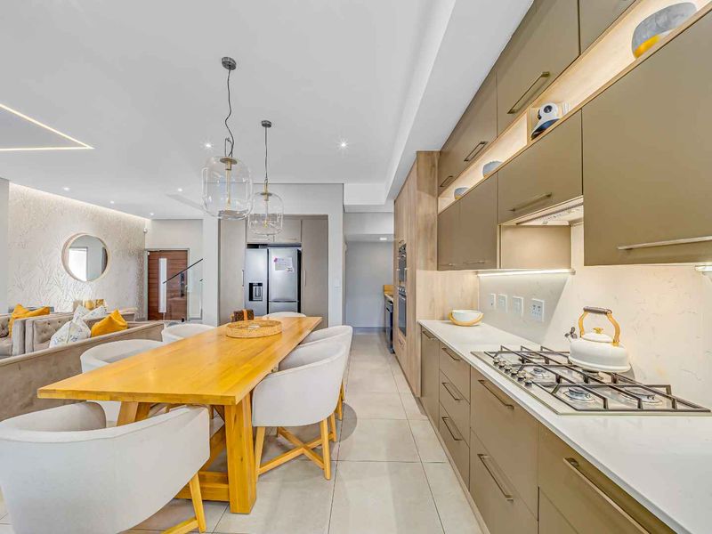 Modern open-plan kitchen and dining area featuring sleek cabinetry, stone countertops, a gas hob, and integrated appliances with contemporary recessed lighting.