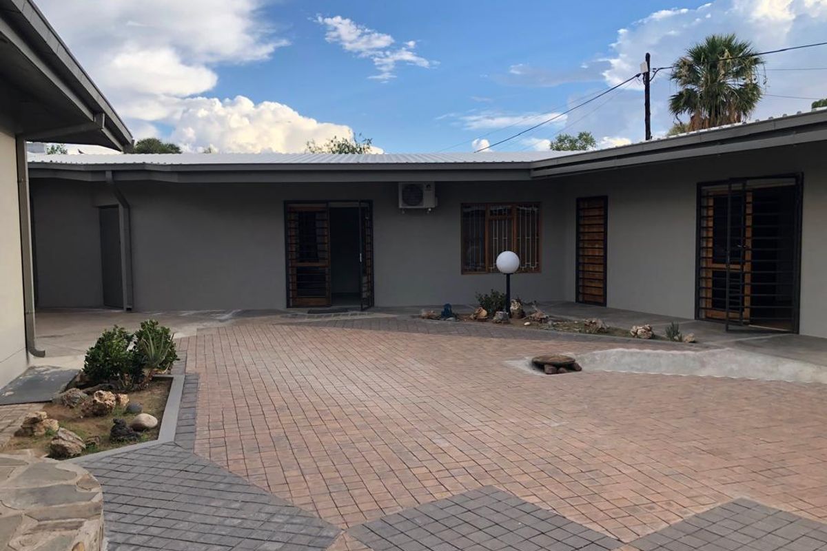 A spacious paved rear courtyard featuring modern grey exterior walls, security gates, and an integrated air conditioning unit.