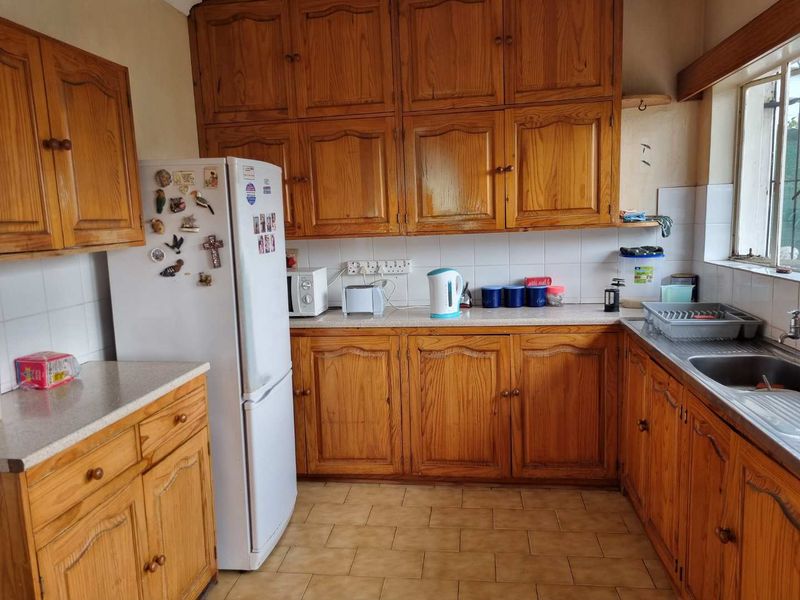A functional kitchen featuring traditional wooden cabinetry, laminate countertops, a stainless steel sink, and tiled flooring, offering a classic layout with ample storage space.