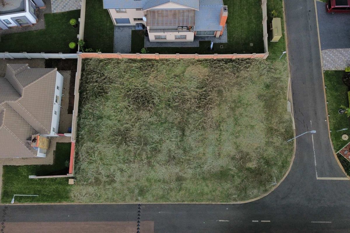 Aerial view of a vacant residential plot situated in a developed estate, featuring established boundary walls and street access.