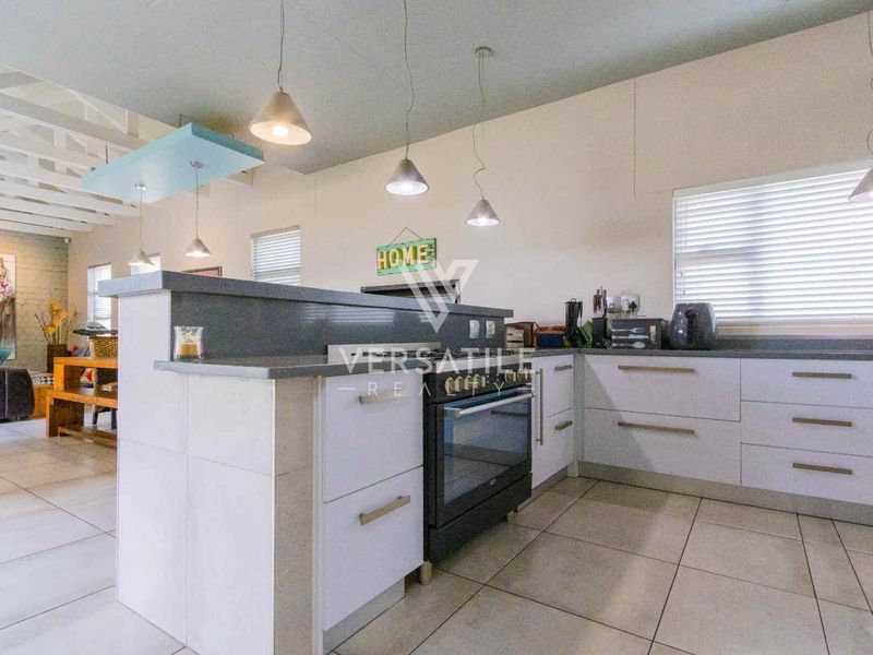 Modern kitchen featuring white cabinetry, stone countertops, built-in oven, and tiled flooring, seamlessly integrated into an open-plan living space.