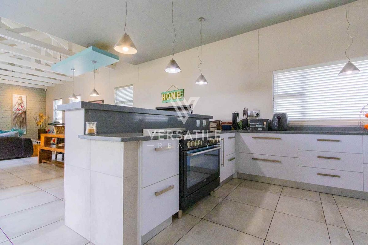 Modern kitchen featuring white cabinetry, stone countertops, built-in oven, and tiled flooring, seamlessly integrated into an open-plan living space.