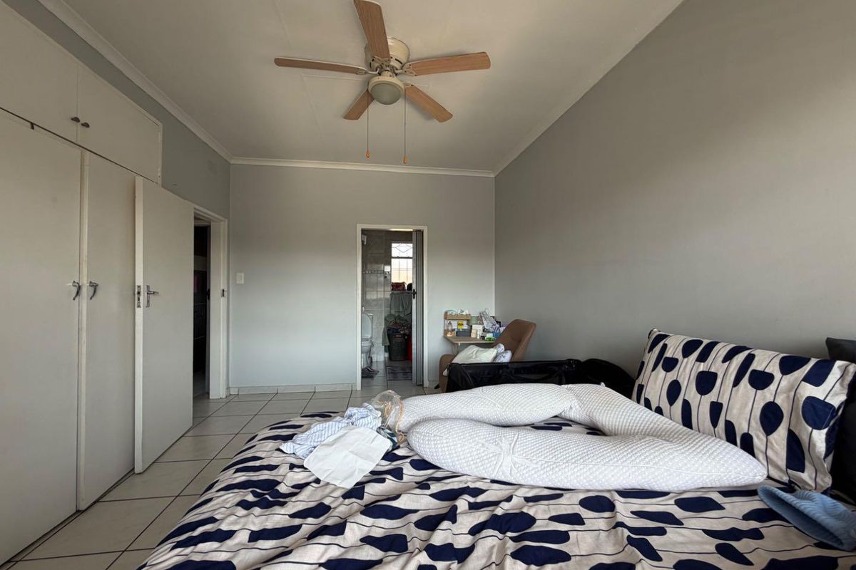 A bedroom featuring built-in cupboards, a ceiling fan, and tiled flooring, with an adjoining bathroom visible through the doorway.