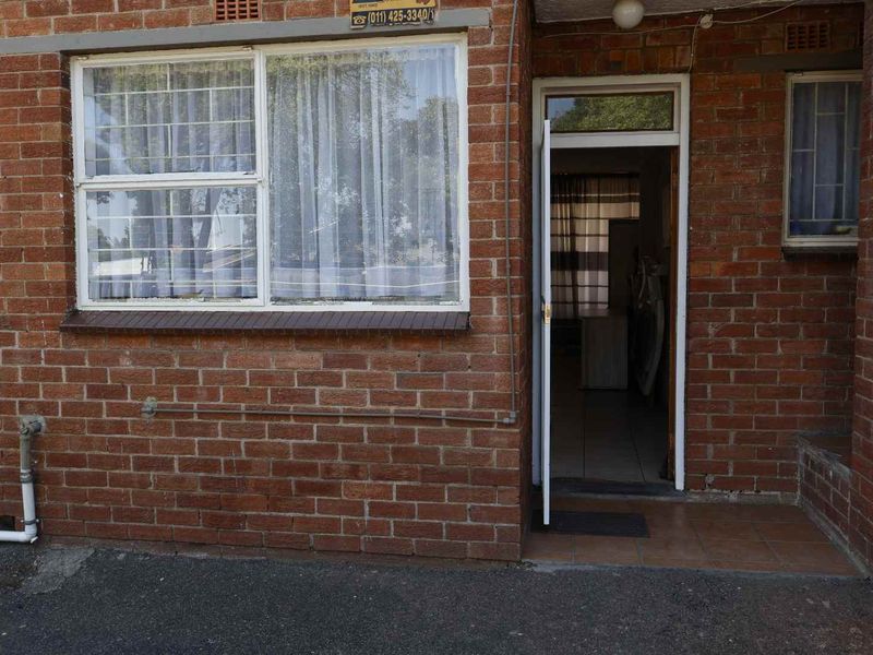 Front entrance of the apartment featuring a classic brick facade, secure window bars, and a tiled threshold.