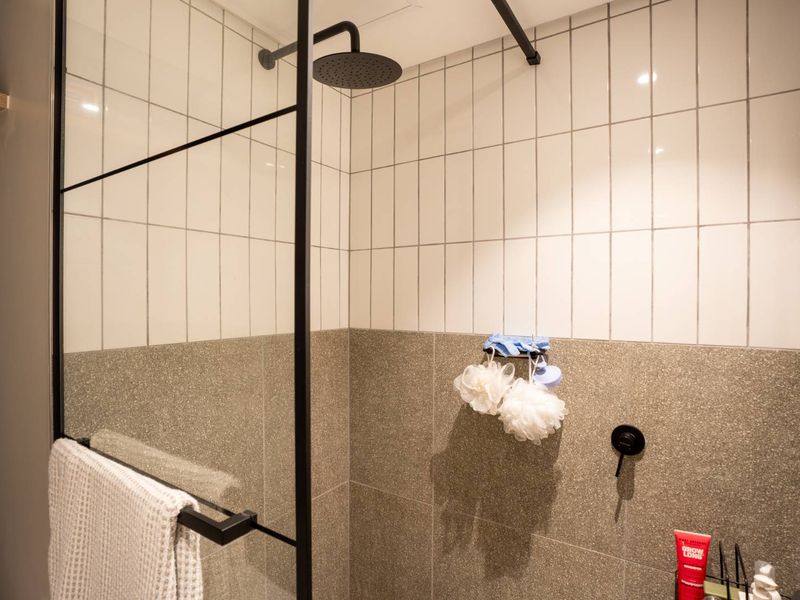 Modern bathroom shower area featuring a sleek black-framed glass screen, rainfall shower head, and a stylish combination of subway and textured stone-look wall tiles.