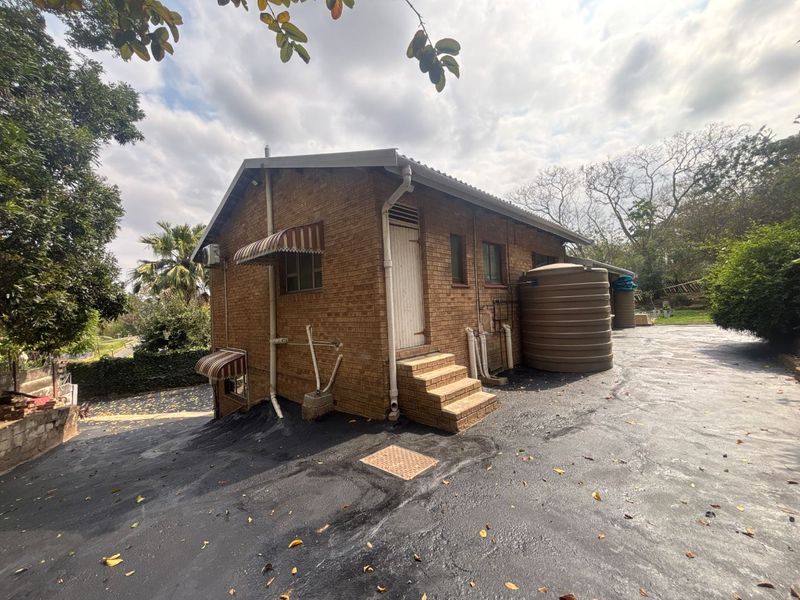 Rear exterior view of the face brick house featuring a large water storage tank, asphalt driveway, and external plumbing fixtures.