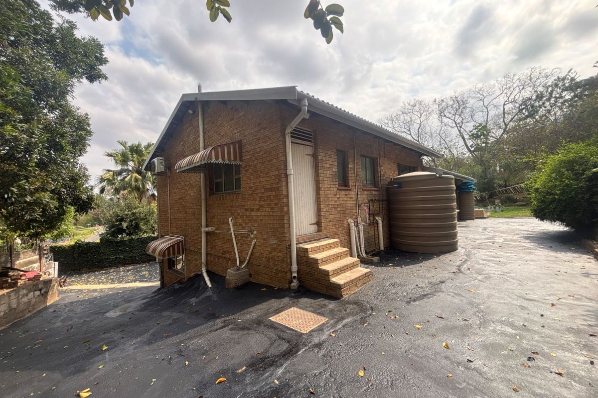 Rear exterior view of the face brick house featuring a large water storage tank, asphalt driveway, and external plumbing fixtures.