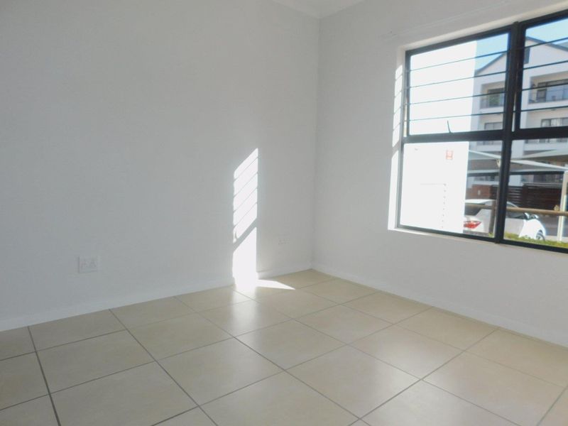 A bright, empty bedroom featuring neutral tiled flooring and a large window with security bars, offering a clean and versatile living space.