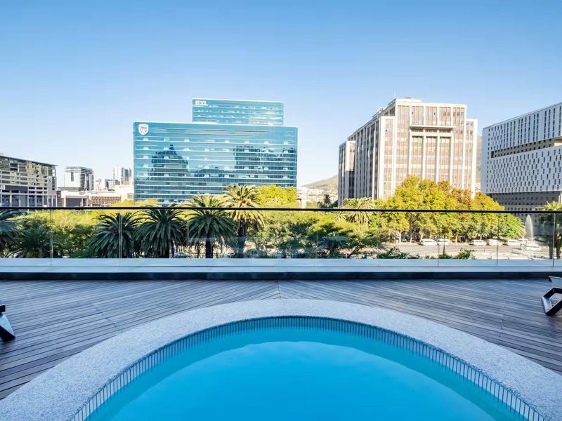 A modern outdoor pool area featuring a circular plunge pool, timber decking, and a frameless glass balustrade with expansive city views.