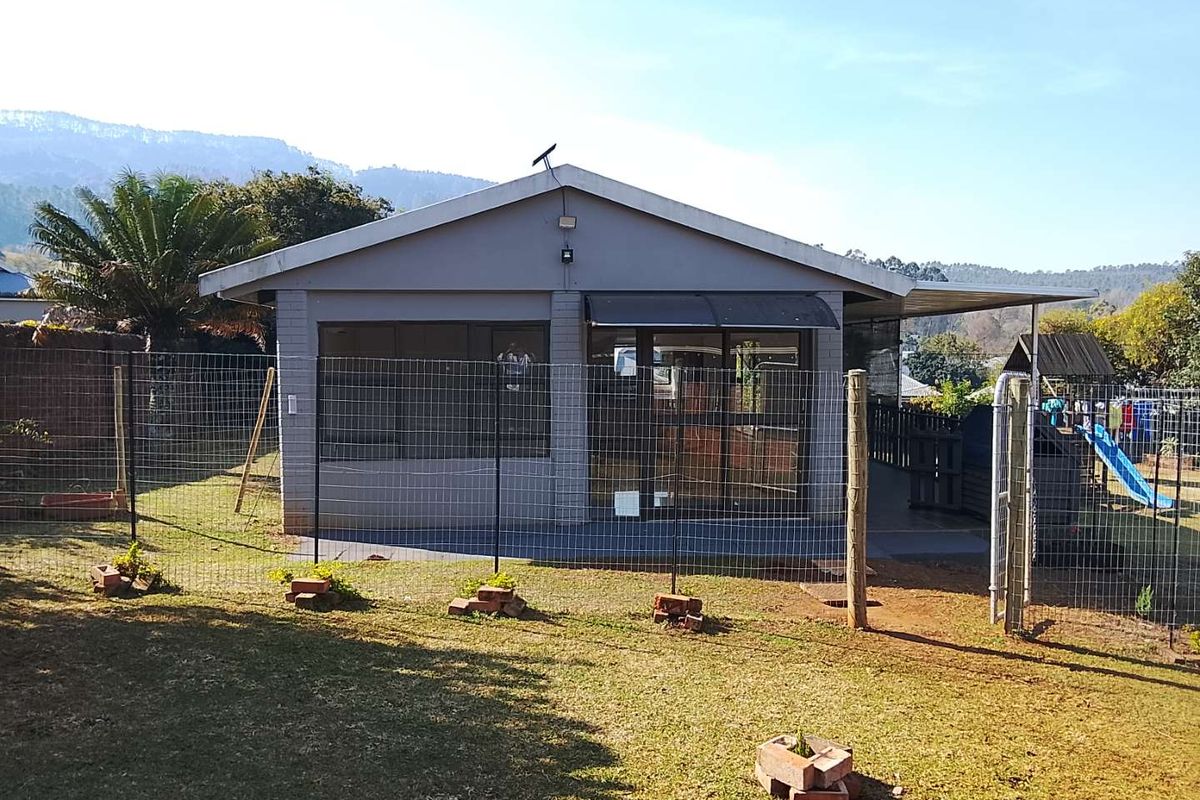 Rear view of the cottage featuring a concrete patio, sliding glass doors, and a fenced garden area with mountain views.