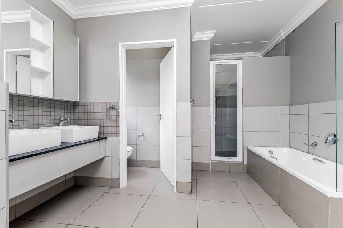 Modern bathroom featuring a double vanity with vessel sinks, a built-in bathtub, and a separate enclosed toilet area with neutral tiling.