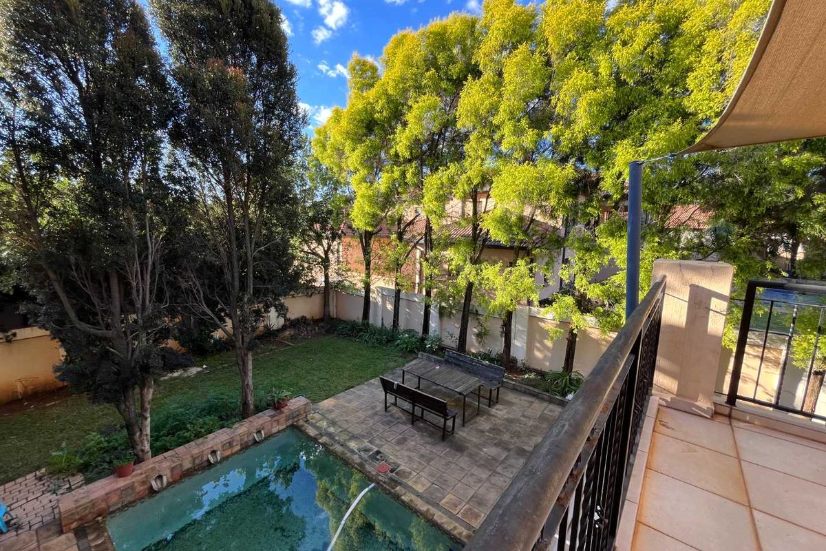 Elevated view of a private backyard featuring a swimming pool, paved patio area, and established garden trees.