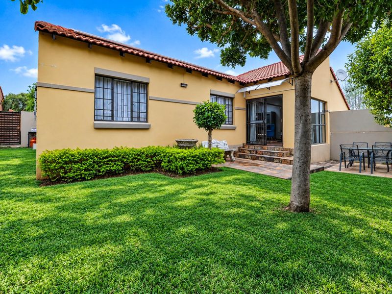 A well-maintained rear exterior view of the townhouse featuring a stone-tiled patio, landscaped garden, and terracotta roof tiles.